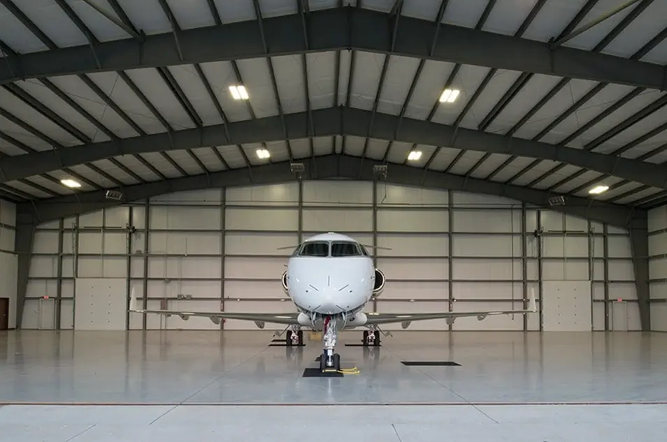 Private jet parked inside a large hangar, showcasing the aircraft's sleek design and spacious interior environment.