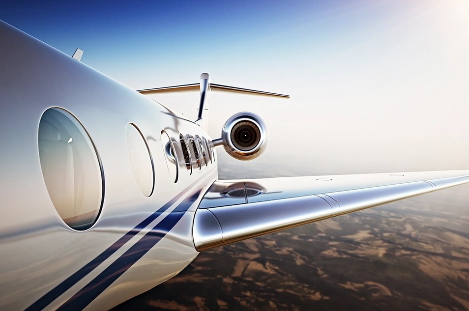 Close-up of a private jet flying over a scenic landscape, highlighting its sleek design and blue sky in the background.