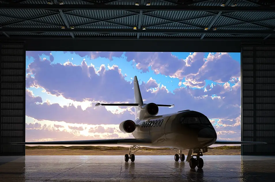 Private jet in hangar with a scenic sky backdrop, ready for takeoff, reflecting sunlight on polished floor.