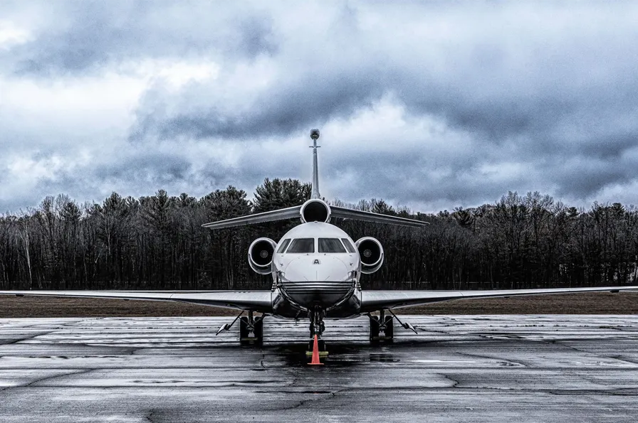 Private jet on a wet runway under overcast skies, surrounded by trees.