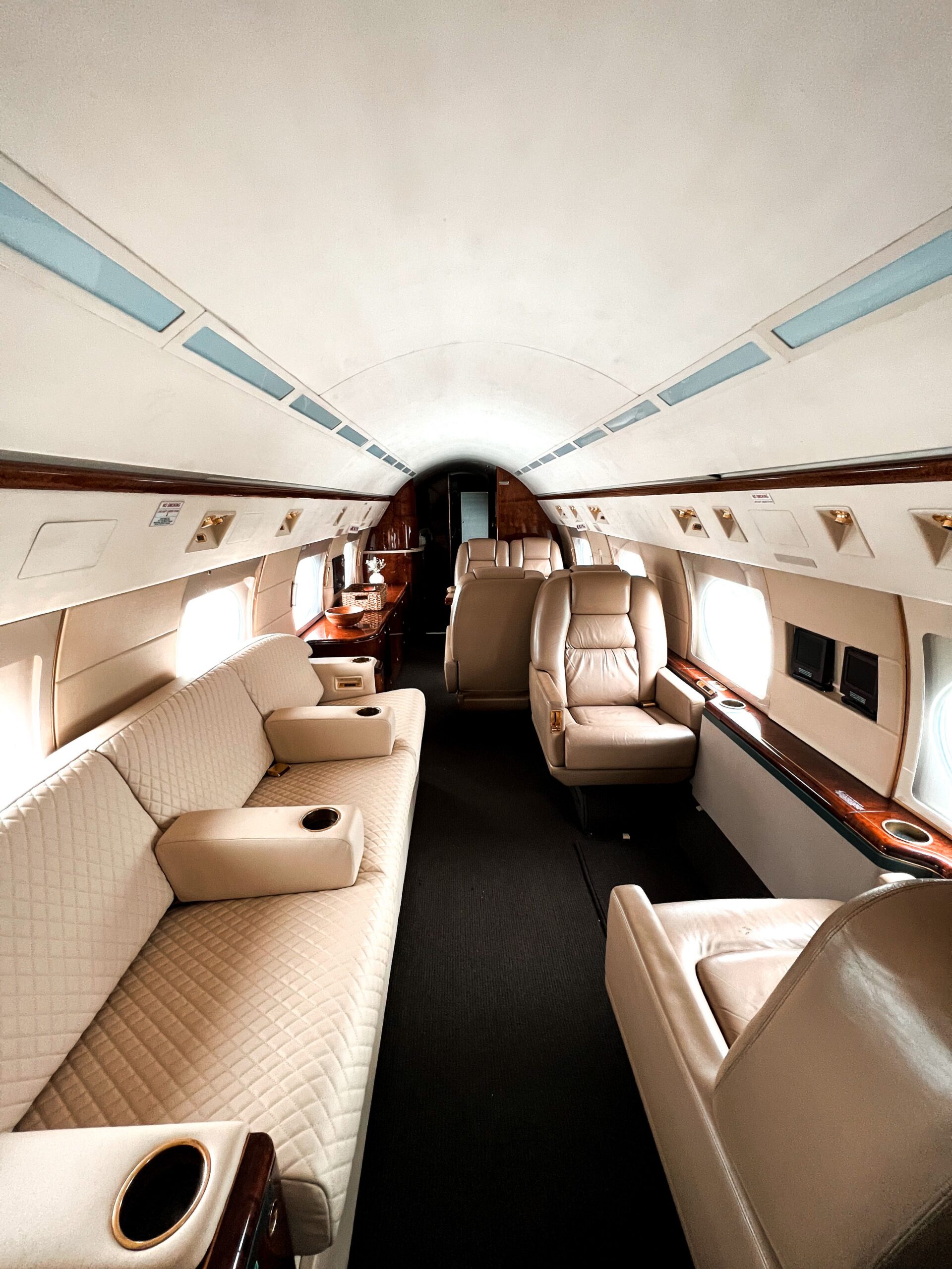Luxurious private jet interior with beige leather seating and elegant wooden accents, offering comfort and style.